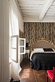 Schlafzimmer mit Balkendecke und opulentem Bett vor Mustertapete
