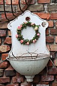 Romantischer Blütenkranz mit rosafarbenen Rosenblüten und Efeublättern an nostalgischem Waschbecken