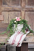 Blumengesteck mit Rosenblüten und Efeuranken auf rustikalem Holztisch