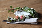 Romantische Tischdekoration mit Rosenblüten und Efeu in Stoffserviette mit Besteck