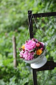 Hydrangeas and roses in vintage-style colander hung from fence