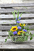 Sunflowers, cornflowers, blades of grass and clematis tendrils in wire basket