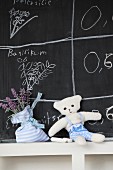Hand-made towelling teddy bear and lavender sachet in front of drawings on chalkboard