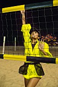 Dunkelhaarige Frau in gelber Designer-Sportkleidung beim Volleyball spielen am Strand
