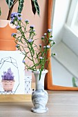 Stems of purple flowers in marble vase in front of mirror and drawing of cactus