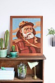 Embroidered portrait of fisherman and cacti on vintage-style wooden shelves