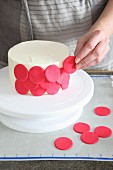 A cake being decorated with red marzipan circles