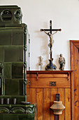 Crucifix on wooden shelf next to green tiled stove