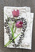 Schachbrettblumen und schwarz verziertes Drahtherz auf Stoffservietten