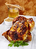 A whole roasted chicken with a honey and mustand glaze showing a dish of mustard and a honey jar and honey drizzler