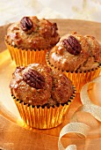 Several Pecan and Maple (syrup) muffins in gold muffin cases on a gold plate with a gold ribbon