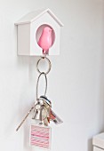 Pink bird key chain pendant hung up in small white birdhouse