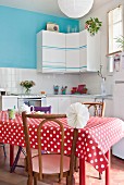 Esstisch mit rot-weisser Tischdecke vor Einbauküche mit dekorierten Hängeschränken