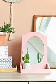 Cactus planted in teacup in front of mirror with pink frame