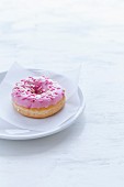 Doughnut mit rosa Zuckerglasur auf weißem Teller