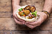 Hands holding a pita bread with falafel