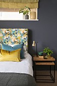 Bed with floral headboard and nest of bedside tables against dark wall