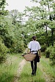 Woman carrying raffia shopping basket along track through woodland