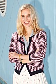 A blonde woman wearing a white skirt, a grey blouse and a striped cardigan