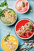Healthy summer breakfast: Colorful fruit smoothie bowls with nuts and oat granola on turquoise blue background