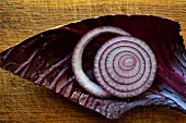 Red, cut onion on a red cabbage leaf on rustic cutting board
