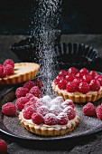 Tartlets with custard, fresh ripe raspberries and sieving sugar powder