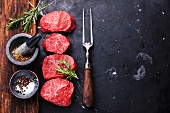 Raw fresh marbled meat Steaks with seasonings and meat fork on dark marble background
