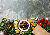 Italienische Zutaten auf Steinuntergrund: Tomaten, Spaghetti, Oliven, Parmesan, Olivenöl und Basilikum
