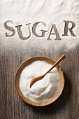 Sugar in a wooden bowl and spilled on a wooden background with the word 'sugar'