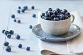 Spotted blue ceramic cup of blueberries with saucer at white textile napkin over wooden table