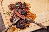 Grilled Ribeye Steak with with knife and fork on meat cutting board on wooden background