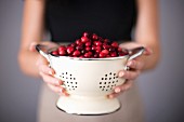 Bright red cranberries in a cream colored strainer being held by a woman