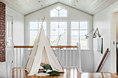 Children's teepee on landing with bank of windows in background