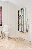 Old window used as shelves hung on wall next to toilet in bathroom