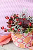 Autumn flower arrangement with rose hips and autumn leaves in pot wrapped in gift wrap
