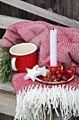 Advent arrangement of rose hips, white wooden stars and candle on fringed blanket