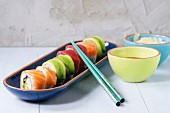Sushi set salmon and avocado rolls served in bright ceramic plates with chopsticks and soy sauce on blue wooden table
