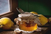 Three juicy quinces, walnuts and jar of honey over wooden table near window