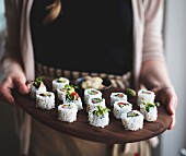 Frau serviert Uramaki-Sushi mit eingelegtem Gemüse auf Holzplatte