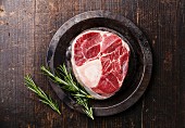 Raw fresh cross cut veal shank for making Osso Buco and rosemary on metal plate dark wooden background