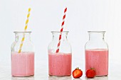 Drei Erdbeersmoothies in Glasflaschen mit Strohhalm