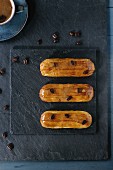 Coffe eclairs with cup of fresh black coffee and coffee beans on black slate board over blue wooden surface