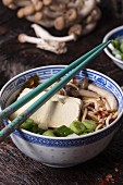 Chinese porcelain bowl of asian ramen soup with feta cheese, noodles, spring onion and mushrooms