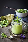 Green gazpacho in jar with peas and lavender on wooden table with vintage colander and spoons