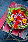 Colourful salad with edible flowers in a bowl on a garden chair