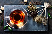 Aufgebrühter Tee in Glastasse und verschiedene Teesorten auf Löffeln