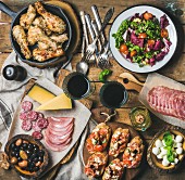 Rustikales Vorspeisenbuffet mit Hähnchenbeinen, Salat, Oliven, Wurst, Bruschetta und Wein