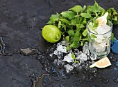Mojito cooking set. Bunch of fresh mint, lime, chipped ice and coctail glass over black slate stone backdrop