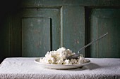 Plate of homemade cottage cheese on white tablecloth with turquoise wooden background