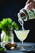 Cocktail mit Gin, Limette und Minze wird aus Cocktailshaker in Glas gegossen